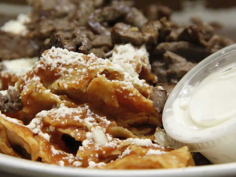 Chilaquiles topped with crumbled cheese, served with a side of sour cream.