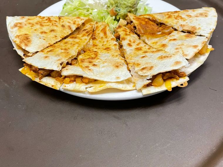 A quesadilla with meat cut into wedges and served with guacamole and sour cream.