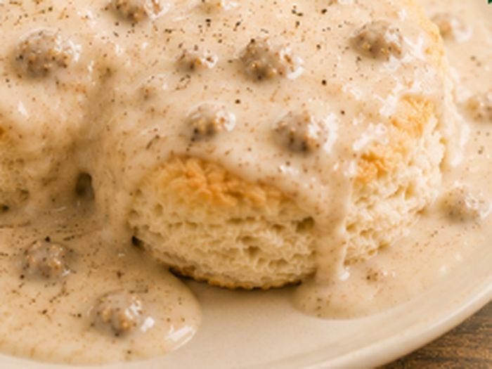 A split buttermilk biscuit under a ladle of Grandma's sausage gravy.