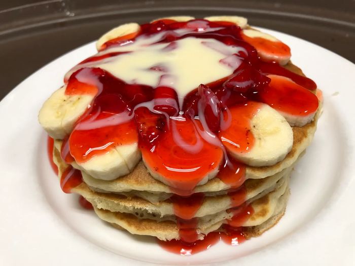 A stack of Mexi Style Pancakes topped with bananas, strawberries and sweet condensed milk.