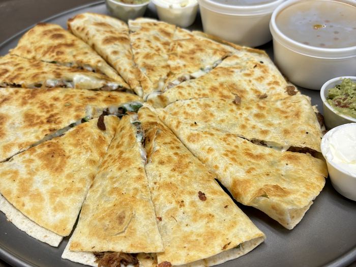 A pizza birria cut into slices and served with cups of guacamole, sour cream and salsa.