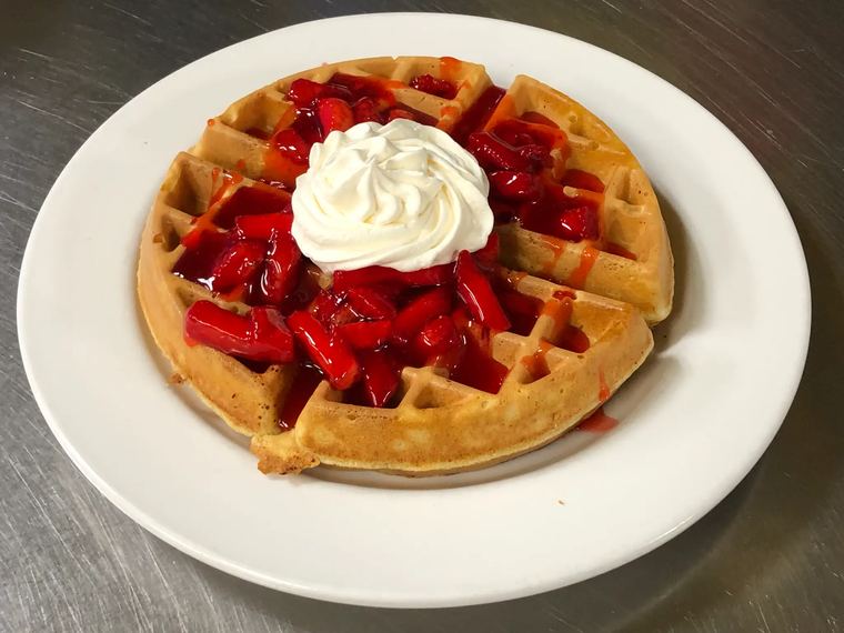 A Belgian waffle topped with glazed strawberries and whipped cream.