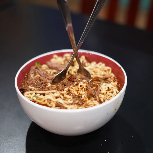A bowl of birria ramen with shredded beef, noodles, onion and cilantro.